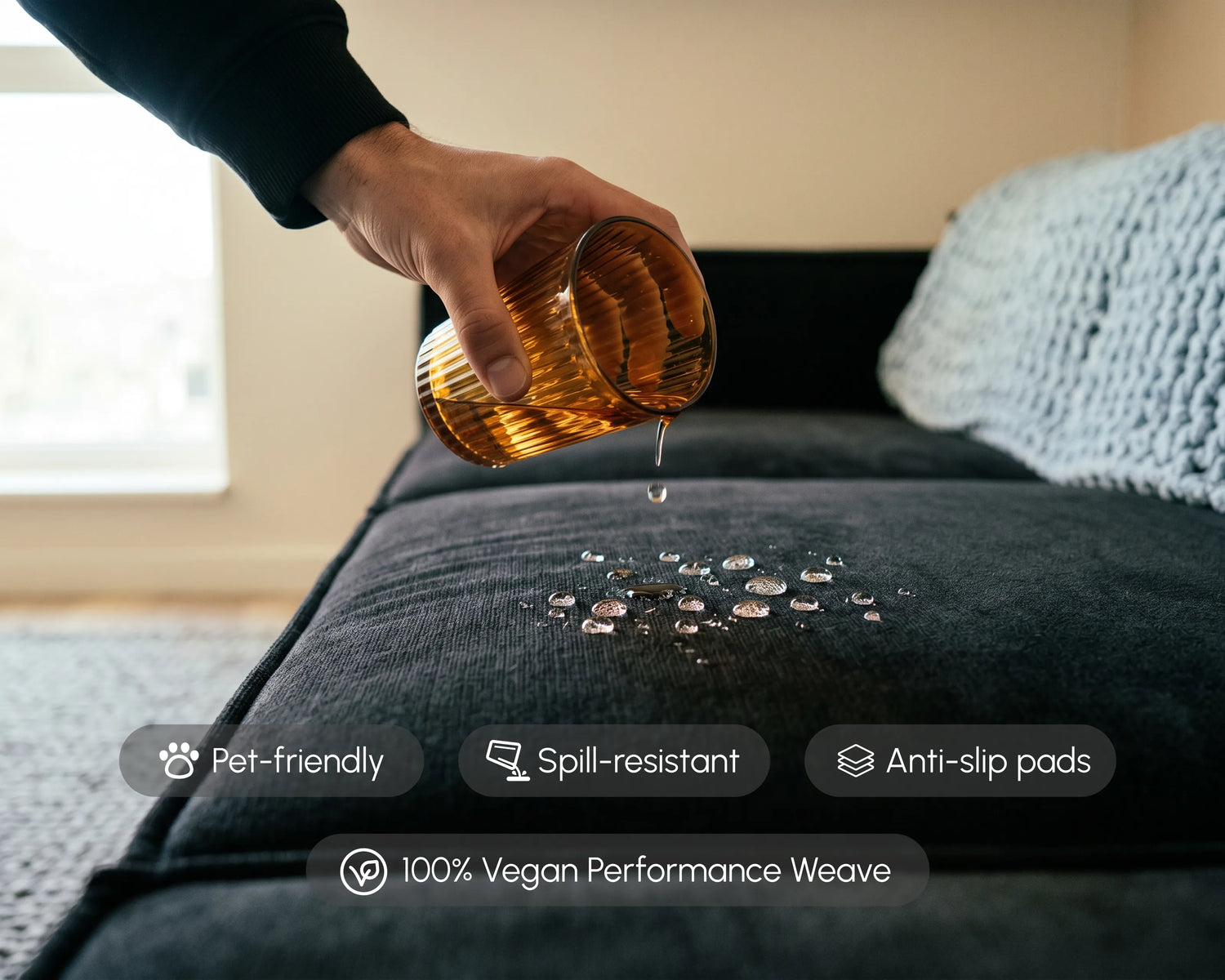 Person pouring liquid onto a black modular sofa with vegan performance weave fabric, highlighting spill-resistant, pet-friendly, and easy-clean living room seating.