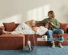 Couple relaxing with a dog on a rust upholstered modular sofa, showcasing soft fabric, spacious seating, pet-friendly comfort, and cosy living room lounging.