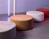 #Assortment of round ottomans in various colors from Rove Lab, set in a modern room with neon lighting accents on a concrete floor